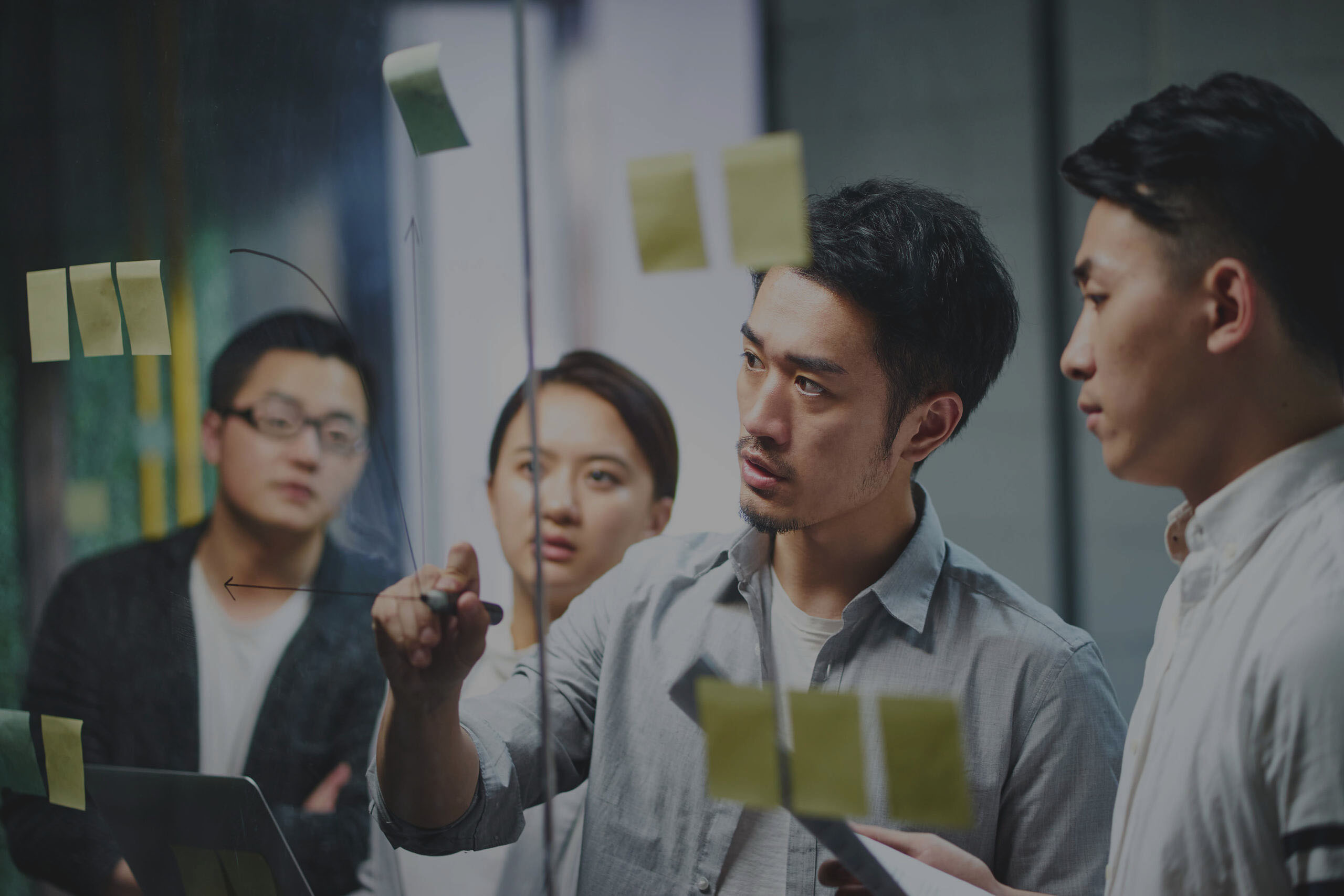 man drawing a chart on glass wall to explain to his coworkers